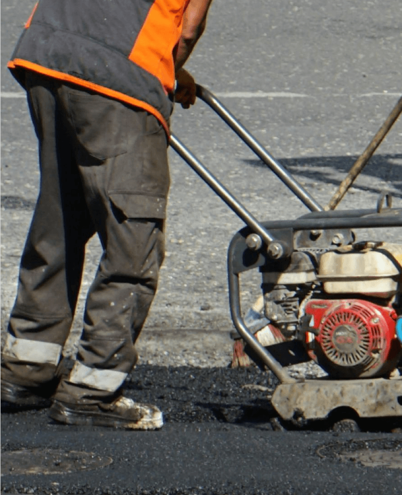 parking lot repair job showing the bottom half of a person using a tamper